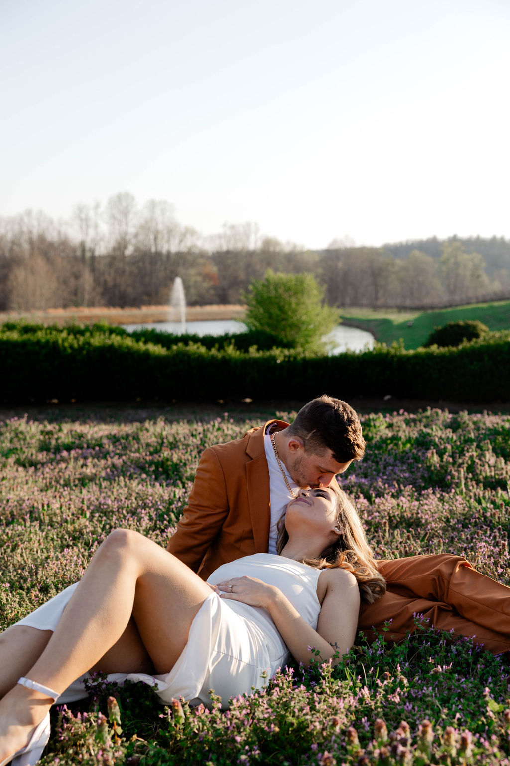 future bride gets a kiss on the forehead lying in a field 
