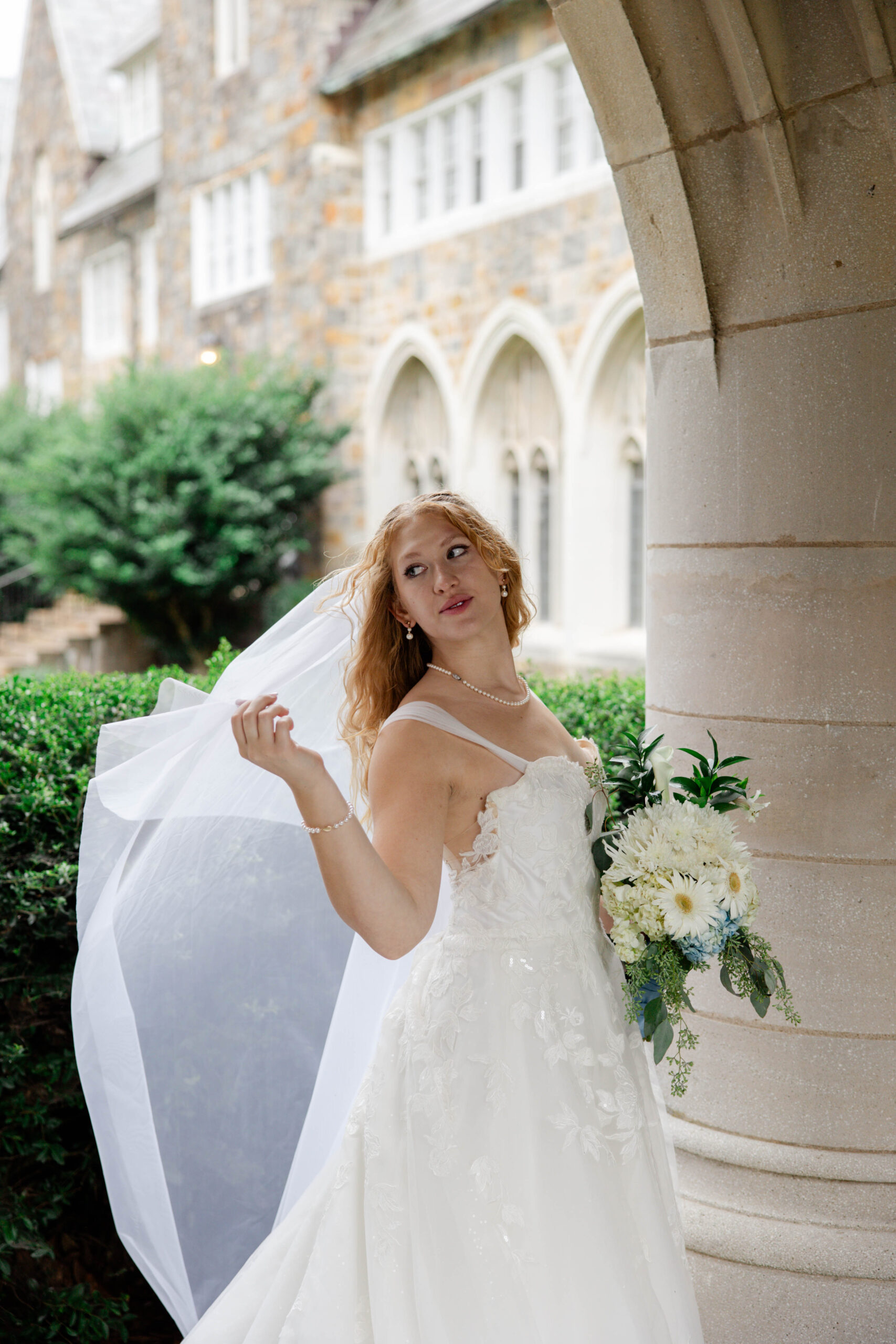 beautiful bride adjusts her veil under the walkway as she handles rain on her wedding day