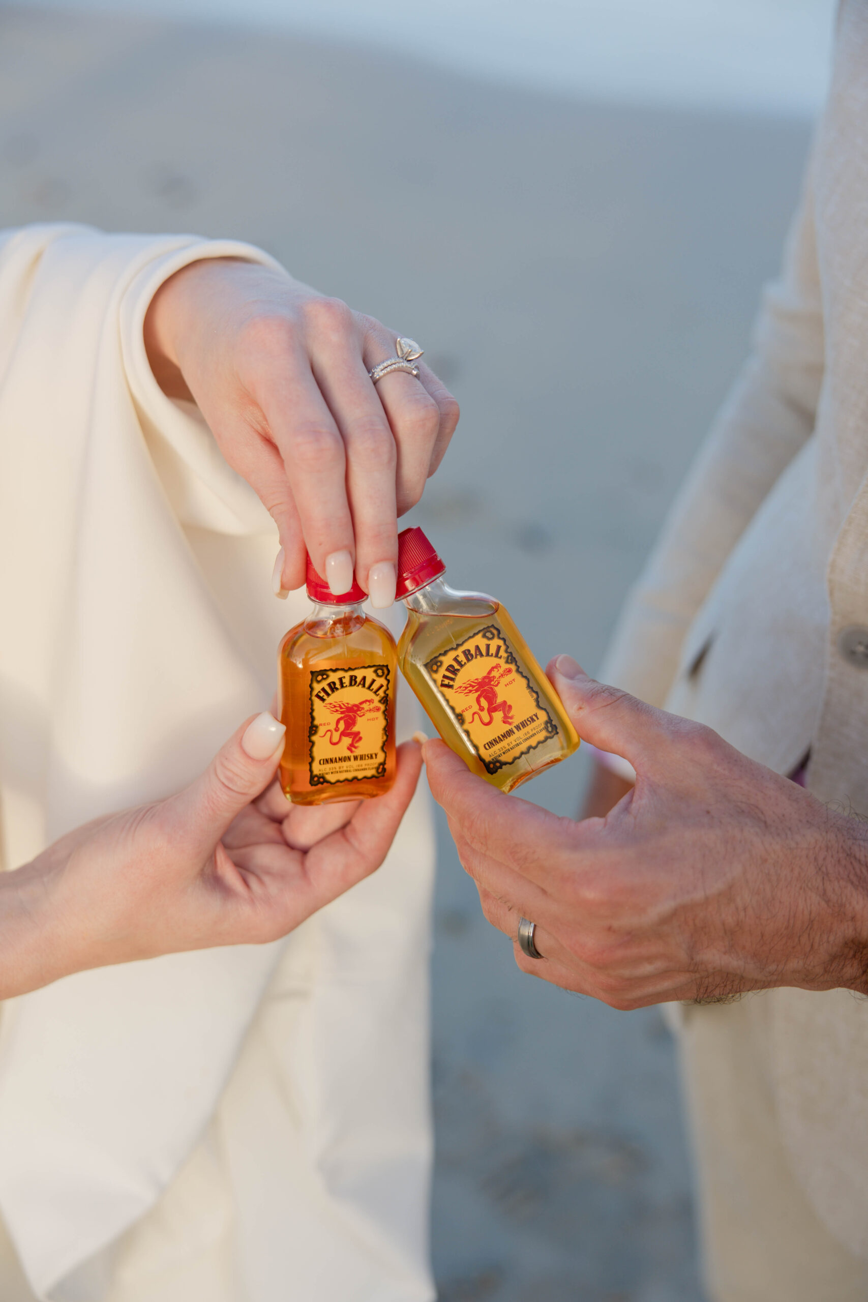bride and groom share shots of fireball on the beach together