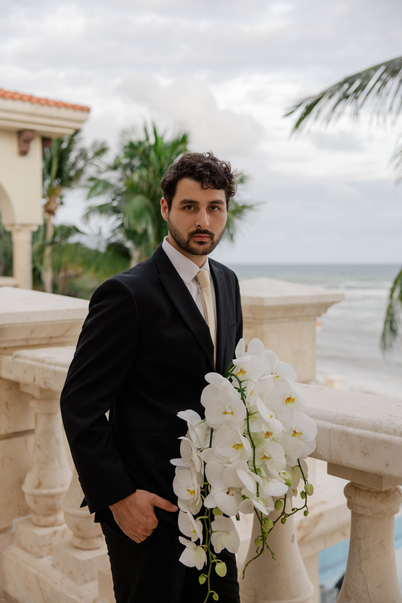 groom poses for a photo with the ocean in the background