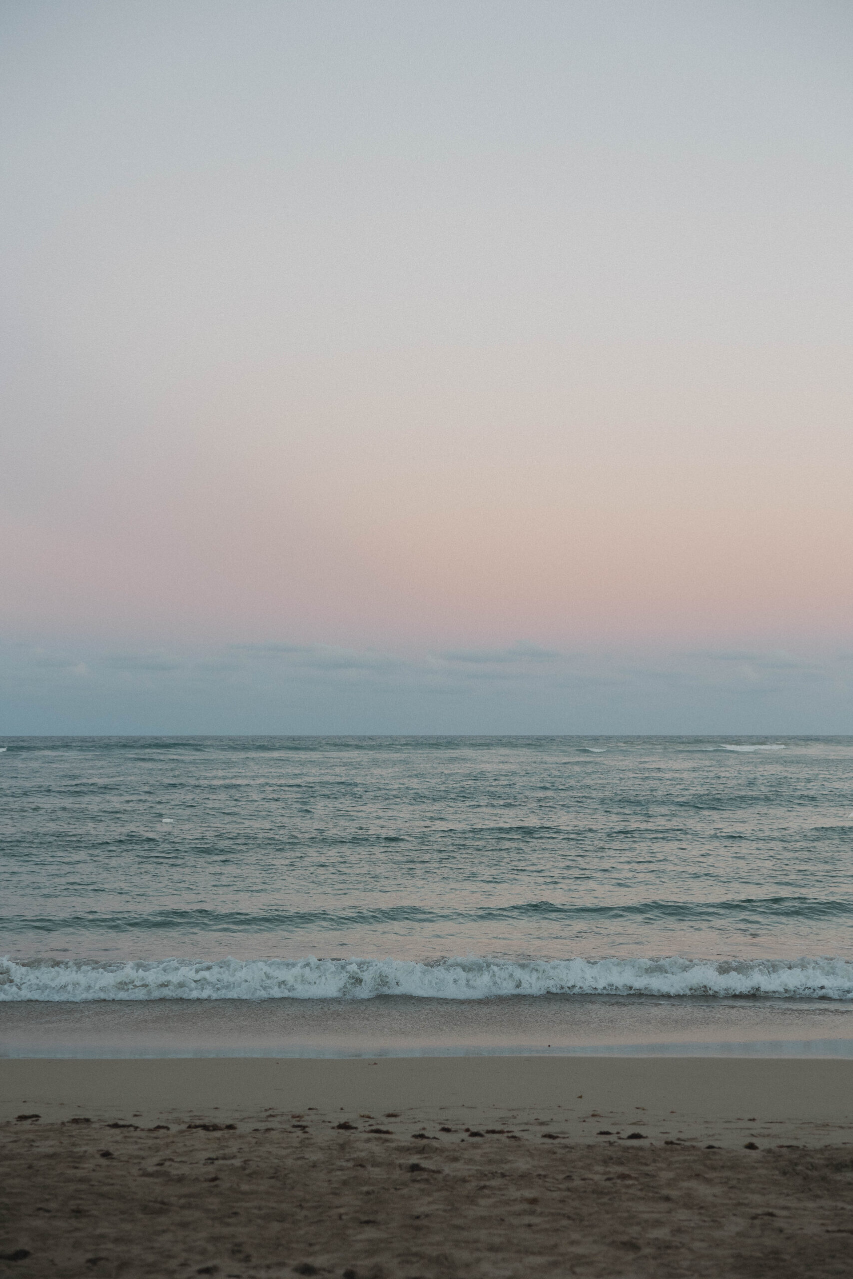 ocean waves roll in under the pastel sunset sky