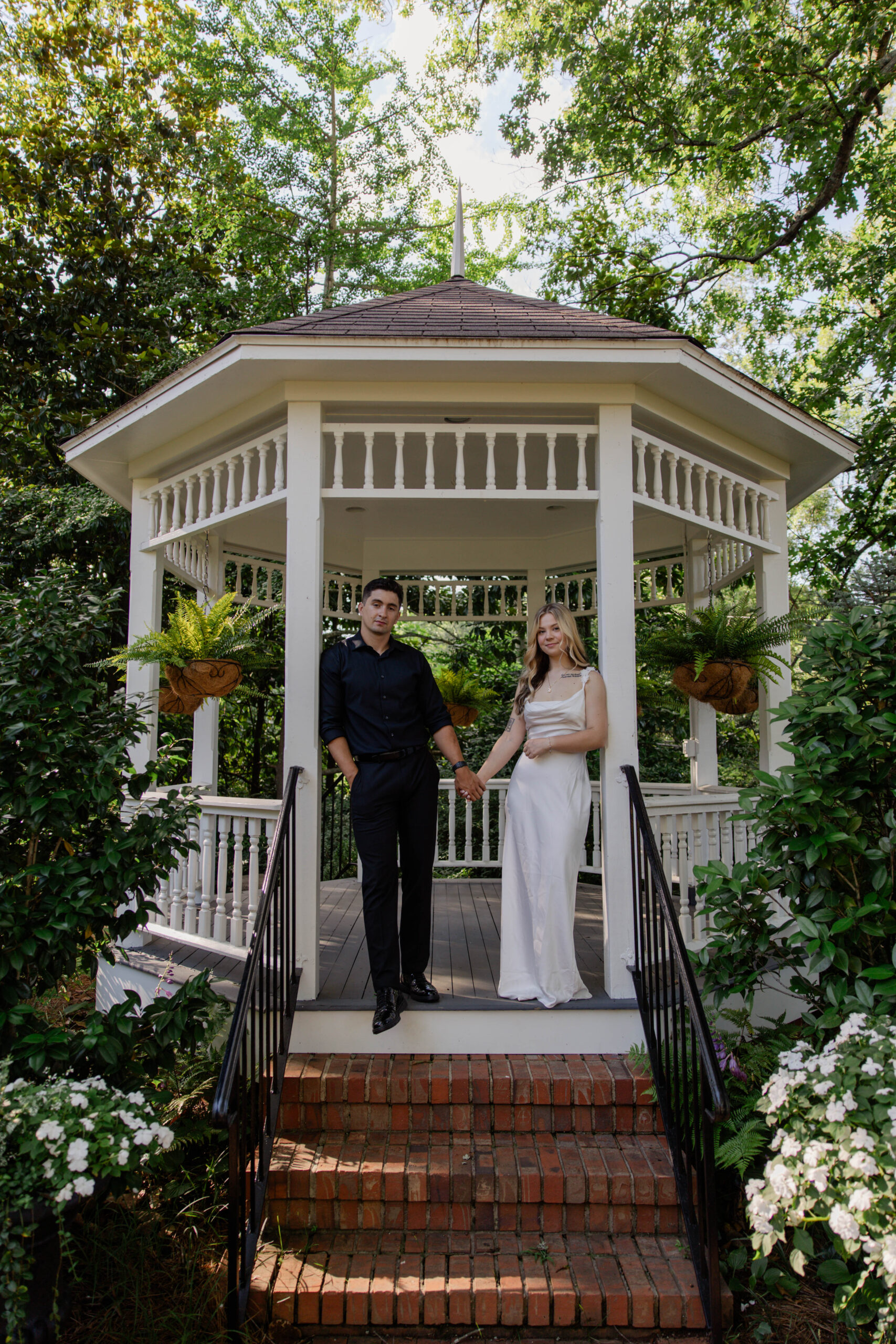 couple hold hands and pose at the entrance to a gazebo, a unique engagement pose idea