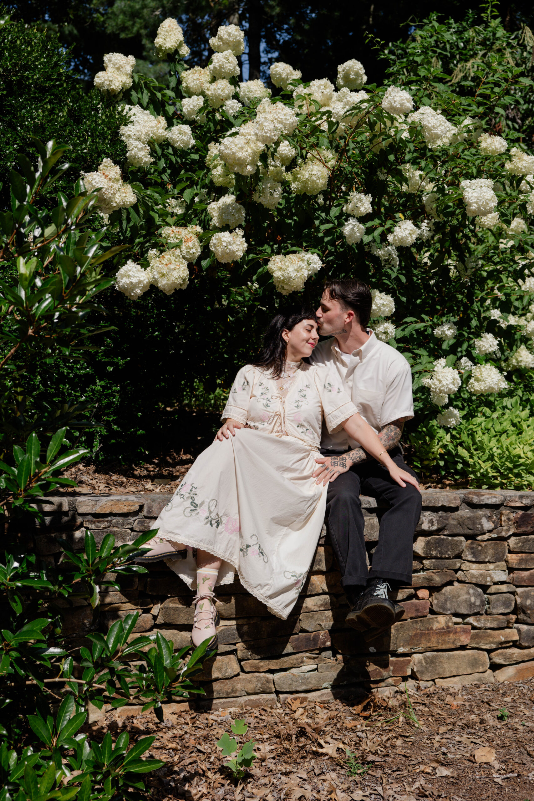 couple share a romantic moment on a wall with a snowball bush standing behind them