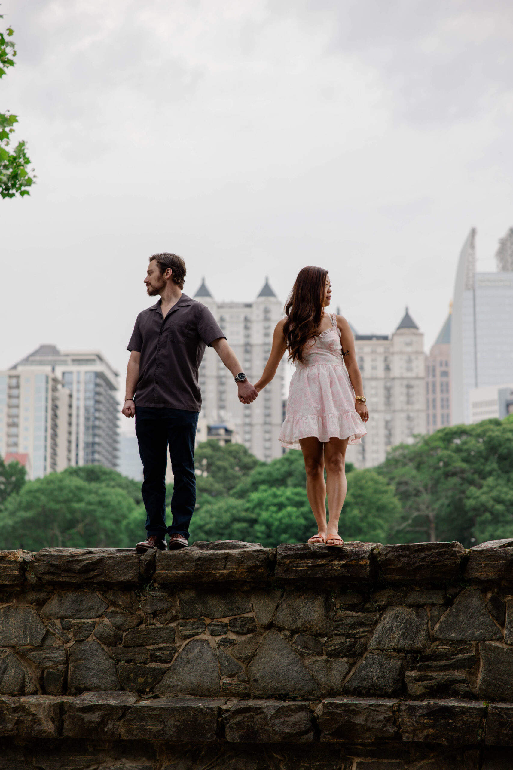 couple stand on a rock wall together with Atlanta standing in the background