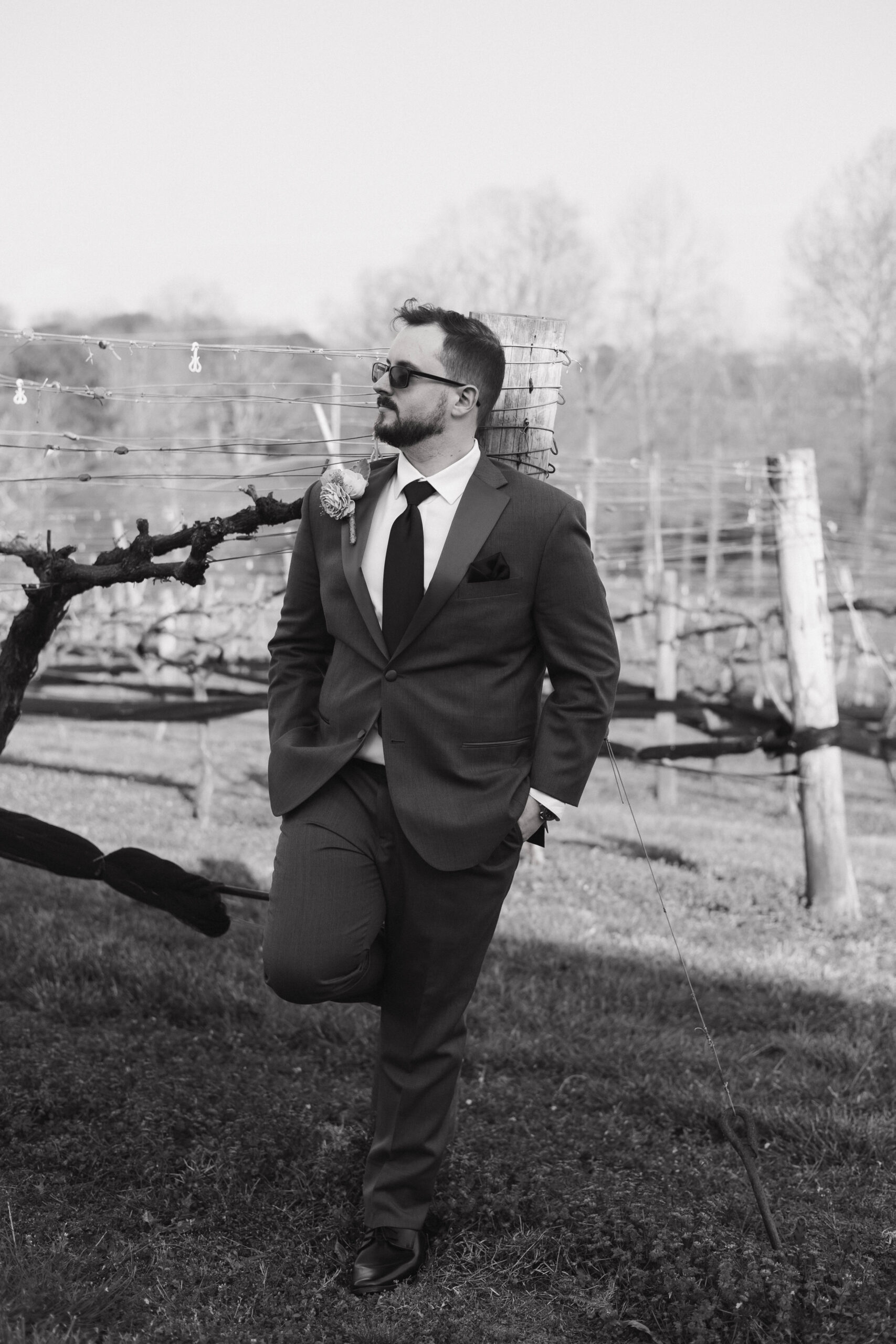 groom poses for a photo against the vines