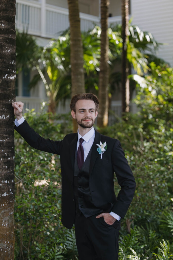 groom poses for a photo against a palm tree after his wedding at isla bella