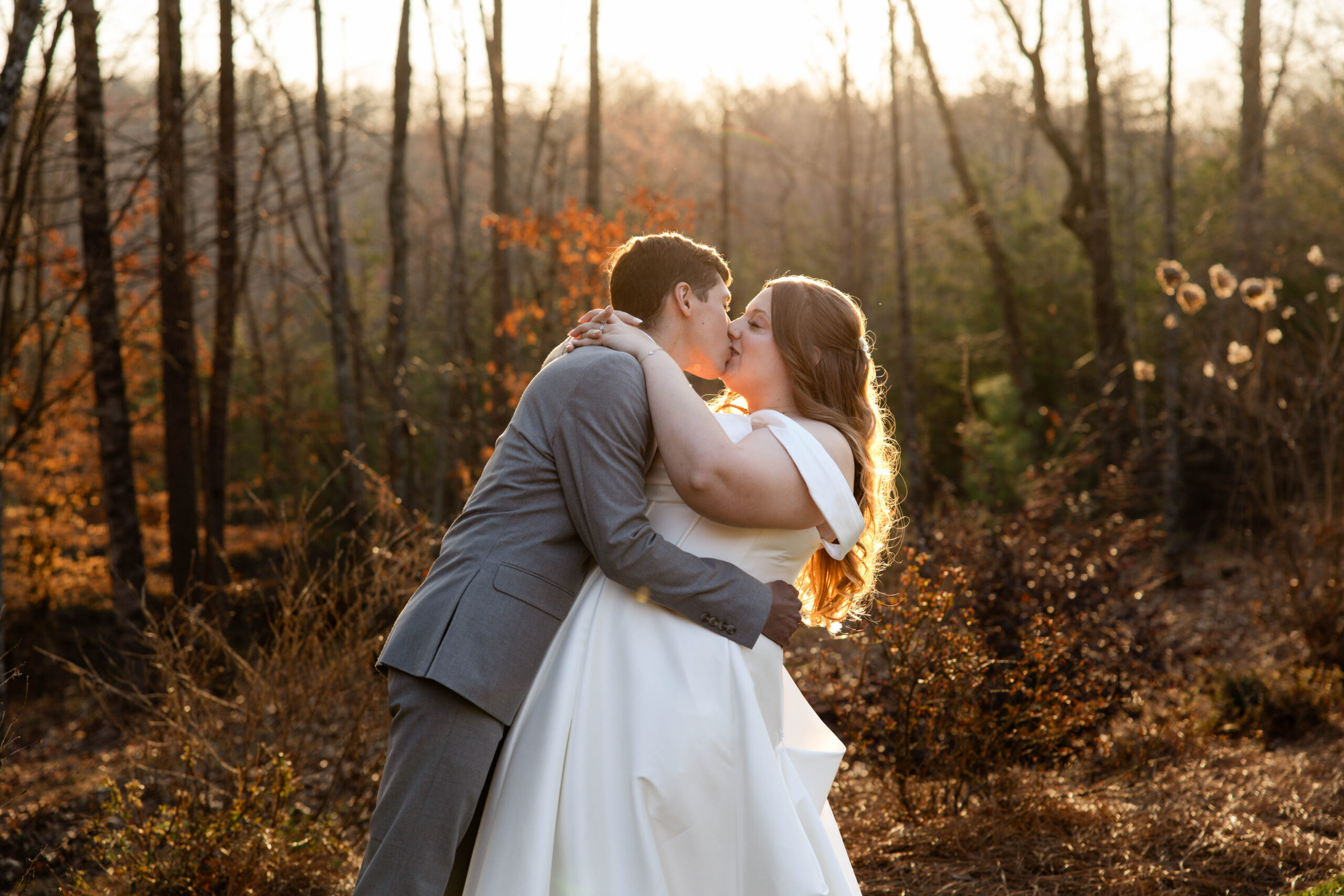bride and groom share a kiss with the fall foliage and sun rays in the background