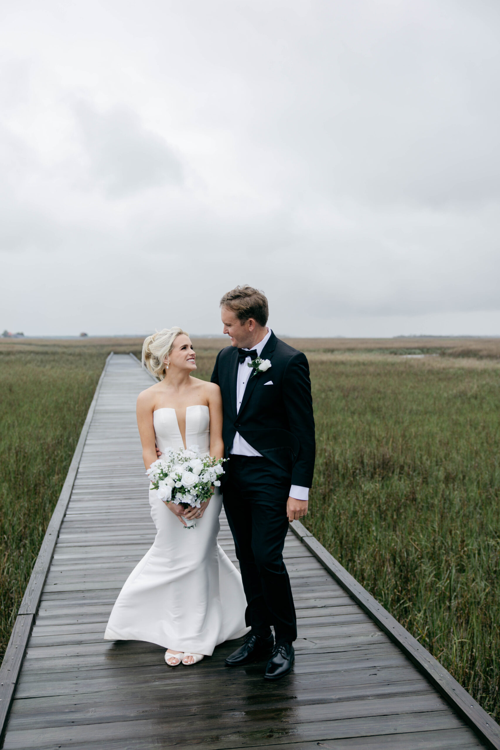bride and groom joke and dance together on the marshland walking path after their Tybee Island wedding day