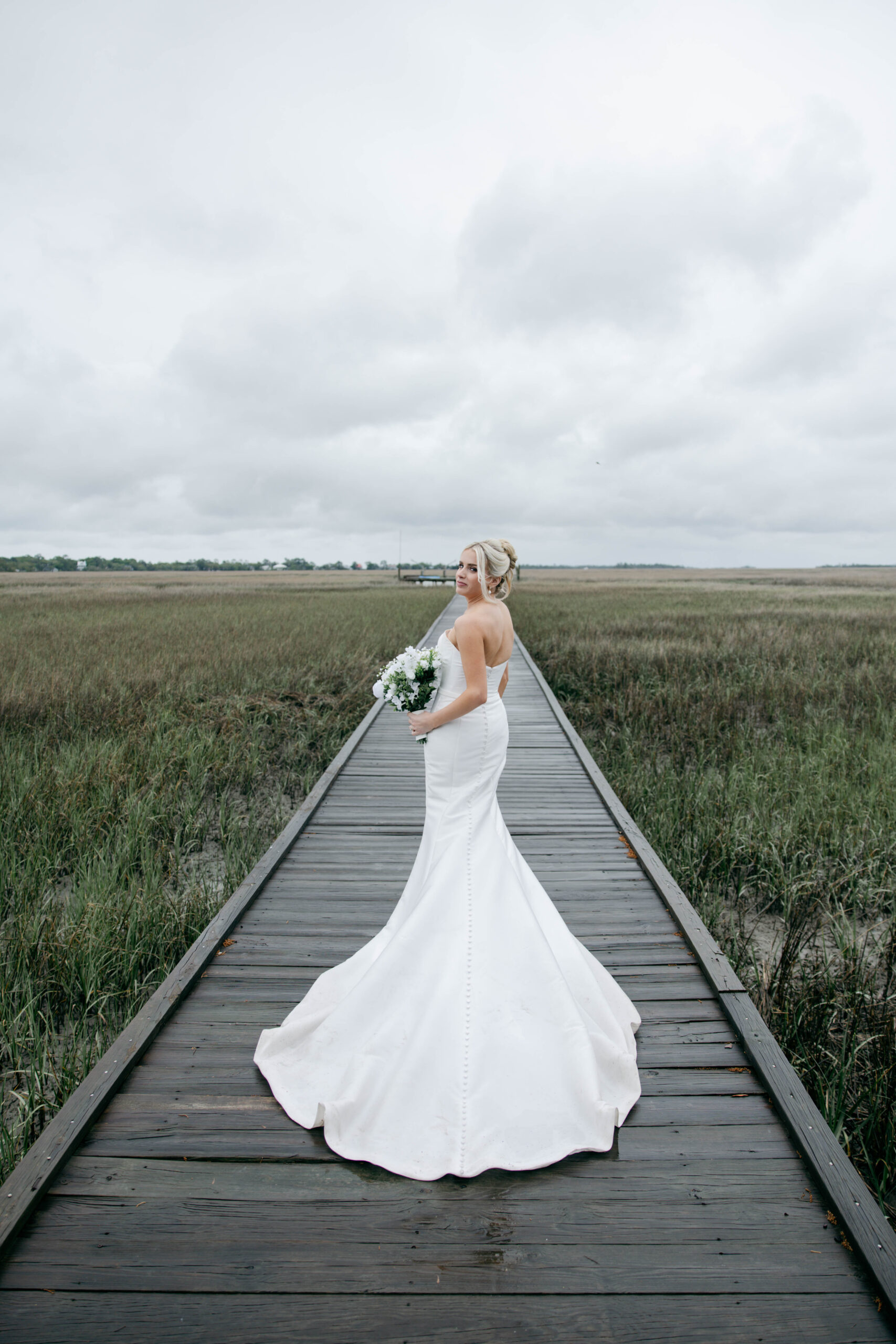 bride poses with her bouquet on the marshy walking path